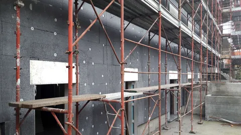 Façade d’un bâtiment en cours d’isolation thermique par l’extérieur, panneaux isolants fixés et échafaudage monté