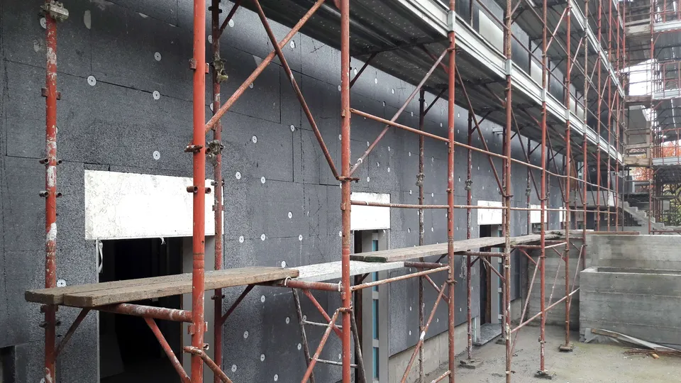 Façade d’un bâtiment en cours d’isolation thermique par l’extérieur, panneaux isolants fixés et échafaudage monté